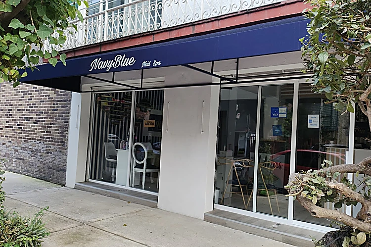 Fachada del salón con toldo azul marino que dice NavyBlue Nail Spa, vidrieras y árboles en la banqueta