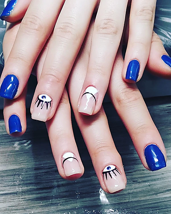 Manos con uñas azul eléctrico y dos uñas nude con un ojo y una media luna pintados