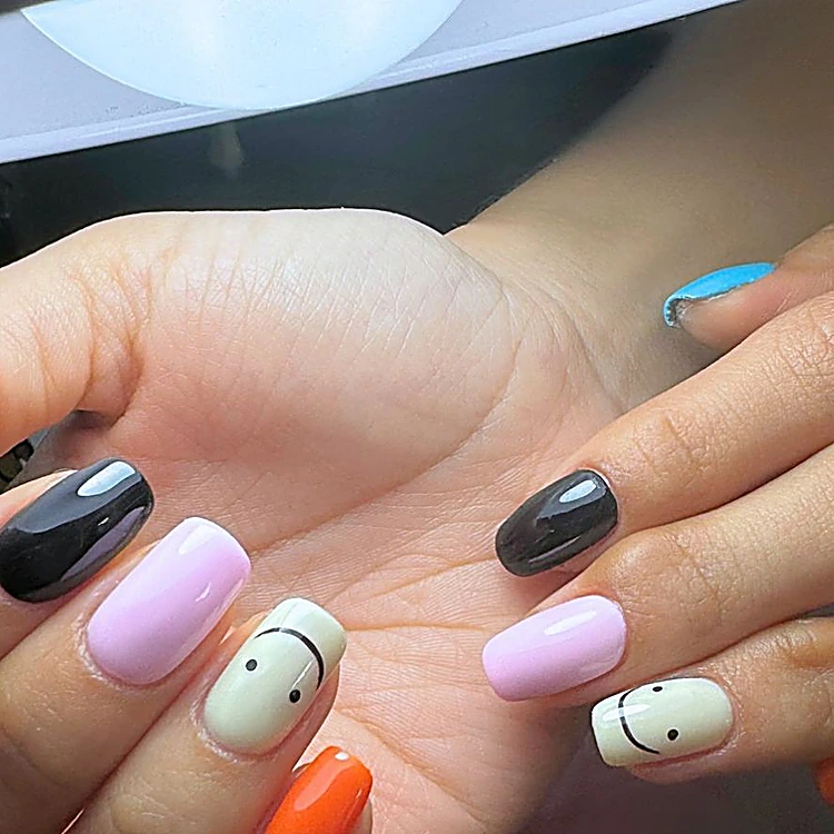 Uñas en negro, lila, naranja y blanco con caritas sonrientes pintadas