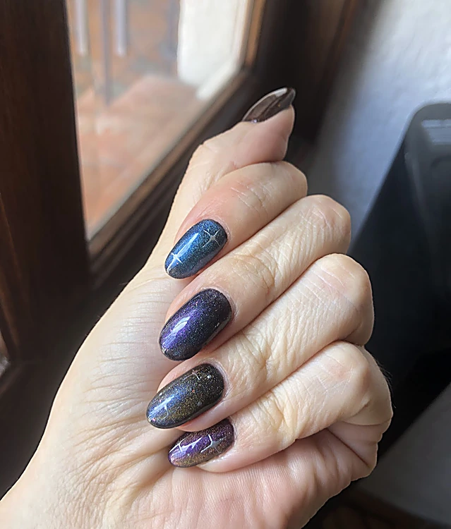 Mano junto a una ventana con uñas efecto galaxia en azul y violeta