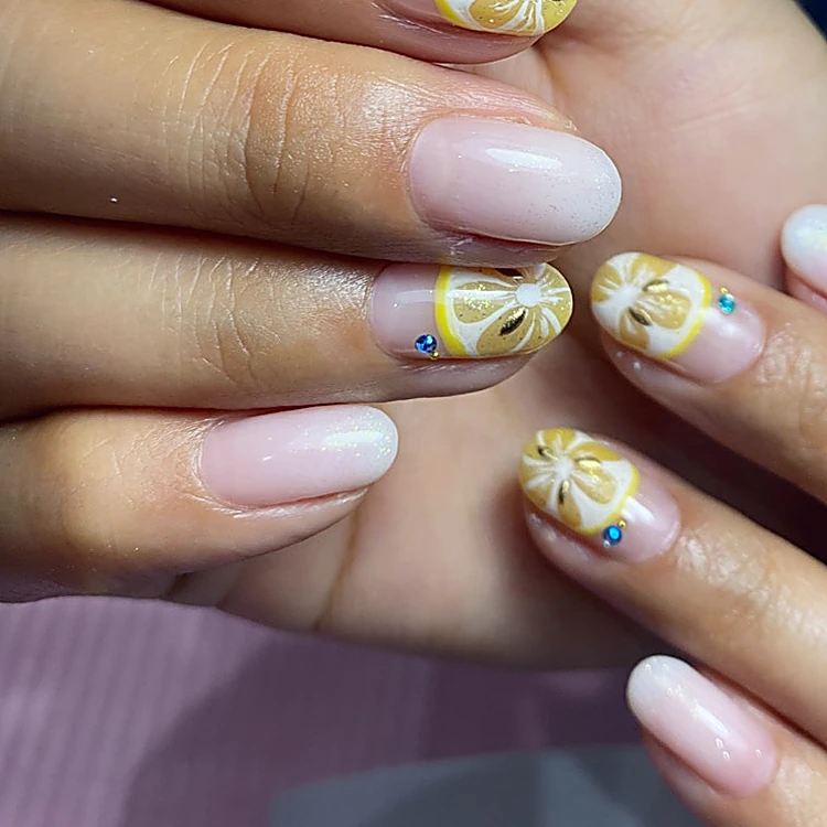 Uñas nude con rodajas de limón amarillas pintadas y piedritas azules